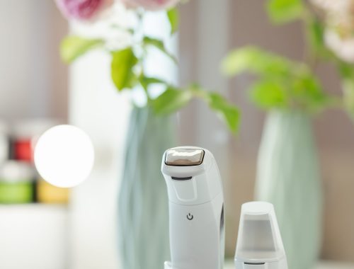 Devices for ultrasonic facial cleansing and massage standing on the table, close up. Mirror and beautiful rose flowers on the background in the beauty salon